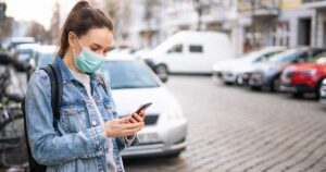 Woman waiting for an Uber on the street wearing a mask.