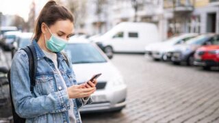 Woman waiting for an Uber on the street wearing a mask.